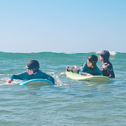 Le moniteur de surf est dans l'eau à hauteur d'homme avec les enfants.